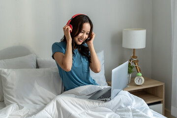 Asian young woman listen to music and using laptop in bedroom at home.