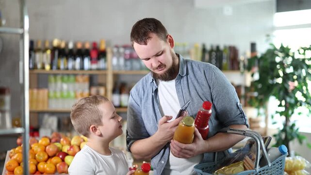 Focused tween boy with friendly young father scanning barcodes on bottles with fruit juices with phone while shopping in supermarket, checking product information and price 