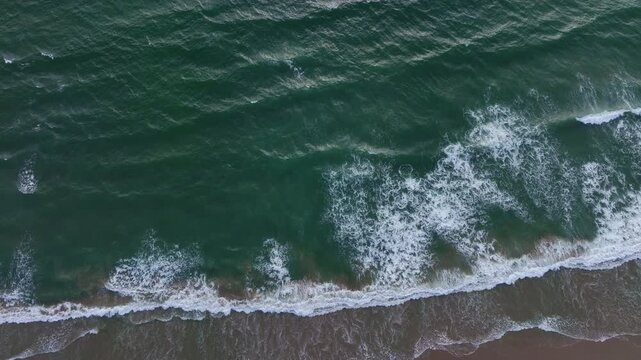 Waves forming white foam. Sea waves in constant motion. Ocean water in motion. Sea waves spreading on sand.