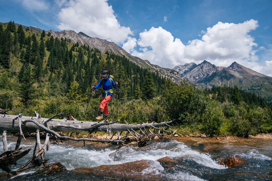 Woman backpacker walking on a one plank bridge in high altitude mountains