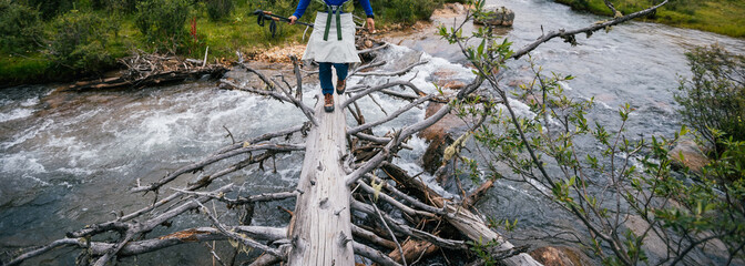 Woman backpacker walking on a one plank bridge in high altitude mountains
