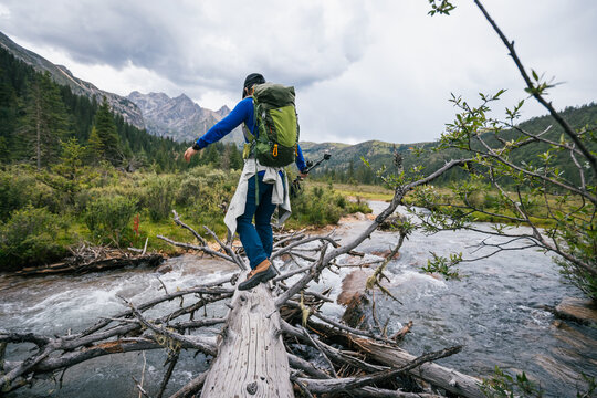 Woman backpacker walking on a one plank bridge in high altitude mountains