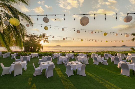 Luxury outdoor beach dinner setup at a tropical resort during golden hour sunset with lanterns. Perfect for destination wedding, event, and travel hospitality concepts