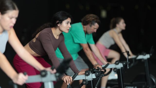 Latin woman came to a group Crossfit workout to build an athletic figure, she does a workout on an exercise bike and actively pedals. High quality 4k footage