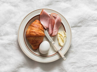 Delicious breakfast - croissant, butter, ham, boiled egg on a light background, top view
