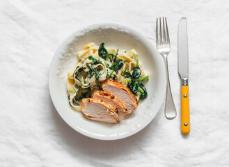 Homemade pasta with cream sauce, spinach and baked chicken breast on a light background, top view