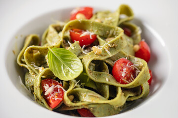 Homemade green tagliatelle pasta with pesto on a plate on the table. Italian cuisine