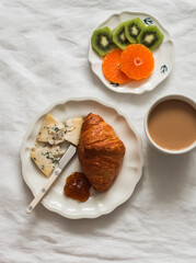 A served breakfast on a light background. Croissant, coffee, cheese, fruit - a delicious start to the day