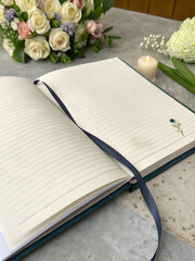 Open condolence book with a ribbon, flowers, and a candle on a marble table