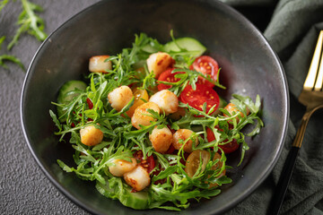 Salad with scallops, cucumbers, tomato cherry and arugula in a bowl on the table. Healthy food.