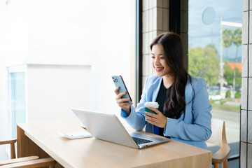 Asian businesswoman using smartphone and laptop in modern office. Professional female entrepreneur multitasking