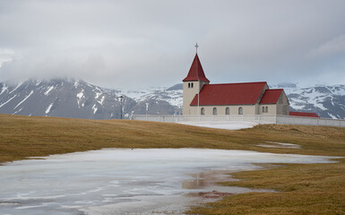 Stadastadakirkja Icelandic church reflecting in melting snow with mountain in background. Iceland