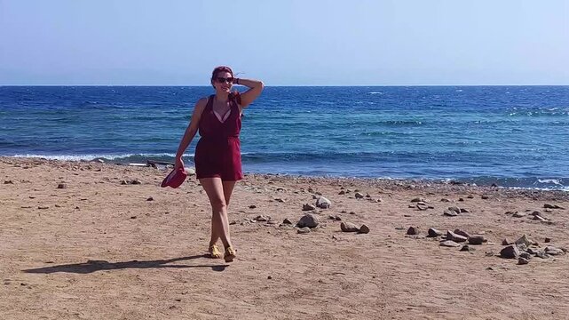 Woman walking along sandy beach holding frisbee with ocean waves in background