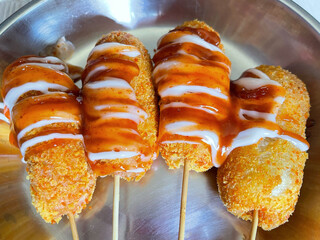 Golden crispy corndogs drizzled with sauce on sticks, popular street food snack concept