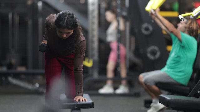 Sportive Latina girl working out with dumbbell in well-equipped gym during weight training session . High quality 4k footage