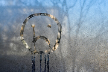 sad smiley face is drawn with fingers on steamy window glass. speaks of loneliness and quiet, introspective moments indoors. Finger art etches sad face into foggy, wet glass pane. abstract background