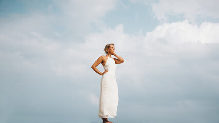 Woman in white dress standing against a cloudy sky outdoors