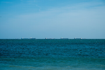a calm blue sea under a clear sky, with several distant cargo ships lining the horizon.