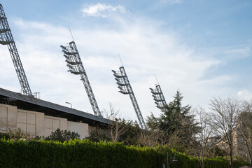 a row of massive angled stadium floodlights mounted on steel trusses, towering over a concrete wall...