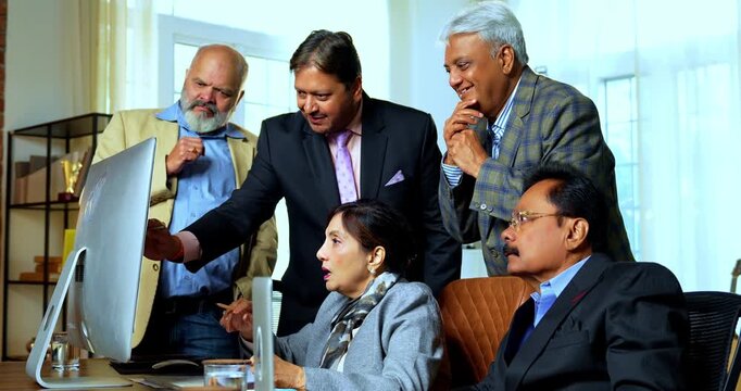 Indian business people celebrating stock market success as senior Indian Asian executives clap, exchange high five while working on laptop computer showing profit during modern corporate office