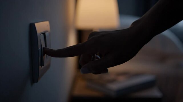 Hand reaching to turn off a light switch in a dimly lit bedroom setting at night