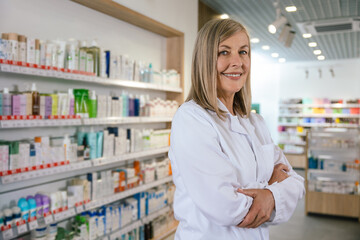 Positive and smiling mature woman in lab coat at the pharmacy