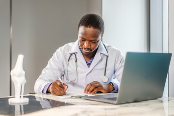 Young doctor man working at office workplace, reading medical record, paper document at laptop, reviewing patient history, sitting at table with laptop computer, working in clinic office