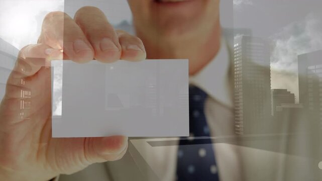 Composite video of mid section of caucasian businessman holing a business card against cityscape