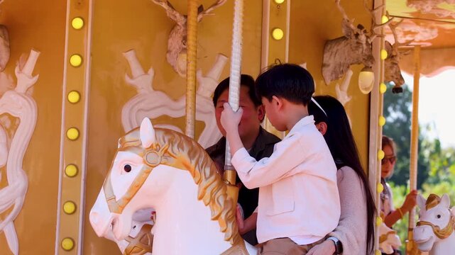 Asian Family with Young Son Enjoying a Carousel Ride at Amusement Park