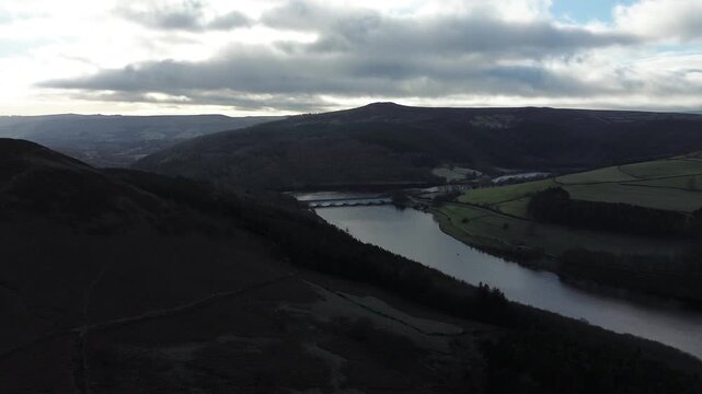 Aerial drone footage panning right across Ladybower Reservoir in Derbyshire, England, showing hills and bridge, suitable for travel, infrastructure, environment and establishing shot use.