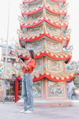 Obraz premium Woman tourist exploring Chinese temple, standing outdoors, capturing traditional architecture details of a colorful pagoda with her camera, enjoying a cultural travel experience
