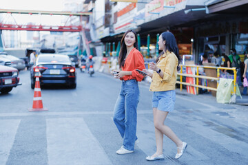 Two young Asian women friends are walking and talking while actively exploring a vibrant street-side market area, enjoying their urban adventure together in a lively city
