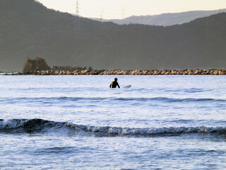 波間のサーファーのシルエットと背後に山々