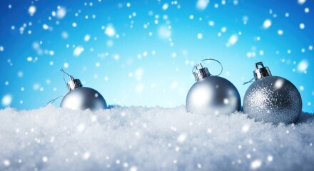 Three silver Christmas ornaments sit nestled in a bed of snow against a backdrop of a vibrant blue sky with falling snow
