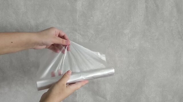 Female hands unwind a roll of plastic transparent disposable bags. Food storage. Use of plastic