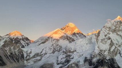 Breathtaking golden hour light bathes the majestic snow-capped mountain peaks, creating a stunning...