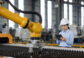 A woman is looking at a tablet while standing next to a robot. The robot is yellow and has a black handle. The woman is wearing a white helmet and a blue shirt