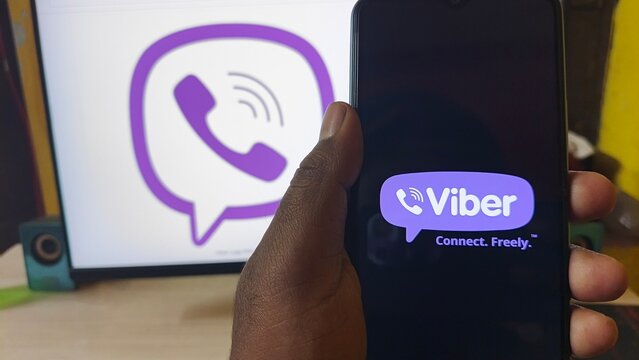 Hand holding smartphone with Viber app in front of WhatsApp logo on computer screen