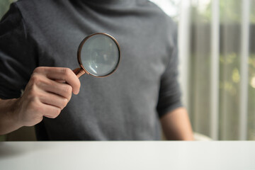 Man holding a magnifying glass over a white table with copy space. Concept of search, focus, data analysis, and quality inspection. Professional discovery tool for business and research projects