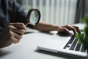 Man holding a magnifying glass over a laptop keyboard. Concept of data audit, online security research, and digital investigation. Professional analysis and finding information tool
