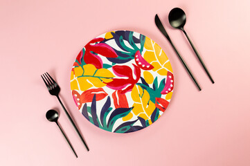 Top view of colorful plate, black cutlery on pink background. Exotic plant plate, summer picnic....