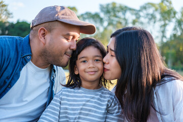 Fototapeta premium Happy asian parents with a child is smiling and playing happy together on the park lawn at sunset on weekend.