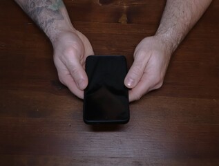 Male hands holding smartphone over brown wooden table