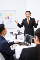 Businessman Confidently Presents To Colleagues In Modern Office Setting With Whiteboard And Laptop