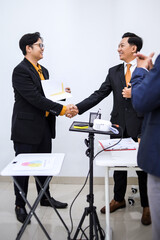 Two Businessmen Shaking Hands In Modern Office Setting With Graphs And Laptop