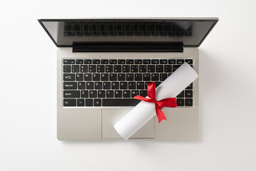 A sleek laptop lies open with a rolled diploma wrapped in a red ribbon resting on the keyboard, symbolizing achievement, study, and the moment of graduation, future career, and educational success