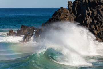 Obraz premium Waves crash against rocks at the mainland's easternmost point, creating rainbows in the ocean spray. Daylight, Byron Bay, New South Wales, Australia.