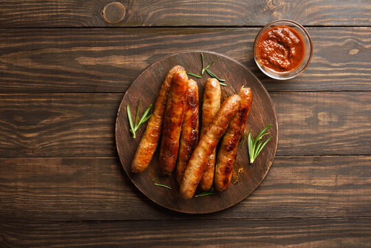 Grilled juicy sausages on platter on wooden background