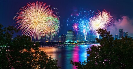 Fototapeta premium City skyline illuminated by vibrant fireworks display. Water reflects colorful explosions, creating beautiful nighttime scene.