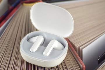 Small white headphones against a background of many books. Audiobook concept